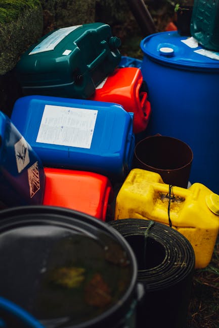 A person wearing a white laboratory coat and tan rubber gloves is holding a bright yellow bin labeled 'WASTES' in a laboratory setting. The bin contains several clear plastic pipettes. In the backgrou